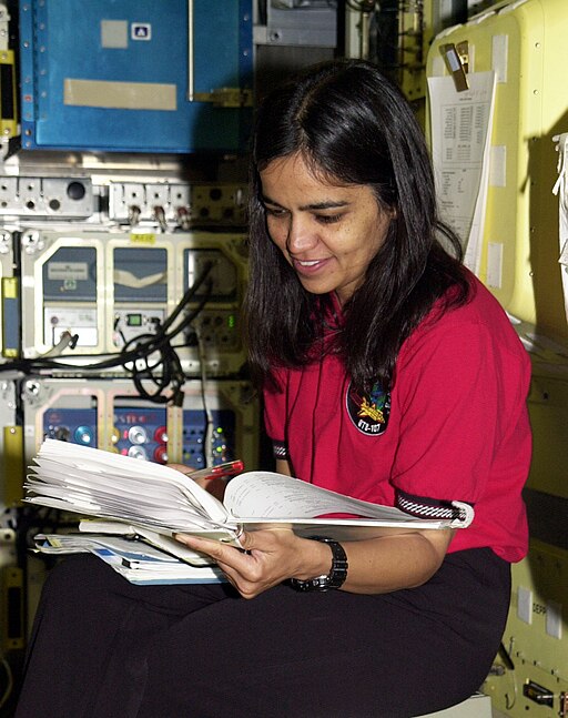 Foto de Kalpana Chawla, pioneira e líder na ciência aeroespacial, sentada nas instalações aeroespaciais da NASA, segurando um caderno aberto.